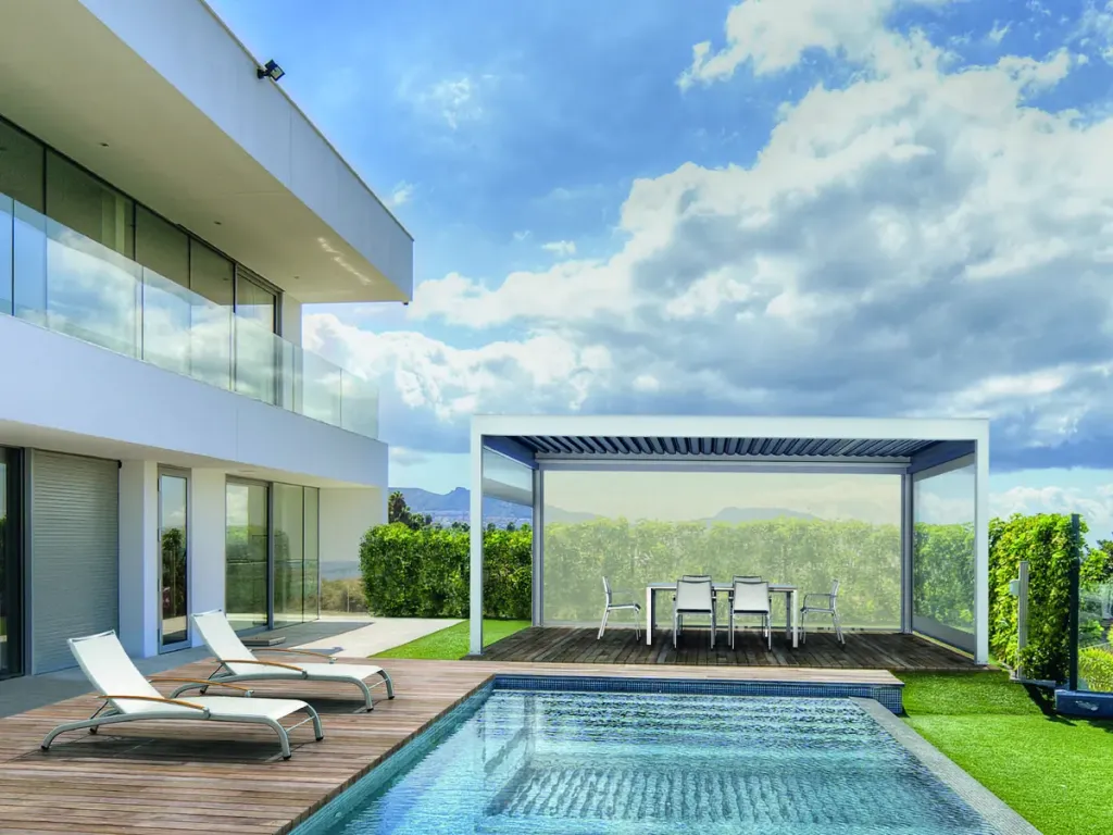 Pérgola cerrada con FlexiZipp junto a la piscina de una casa, con el comedor exterior protegido del viento