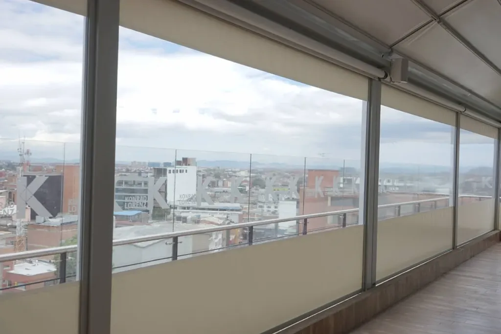 Terraza de oficinas cerrada con FlexiZipp, con las lonas bajadas y la ciudad al fondo