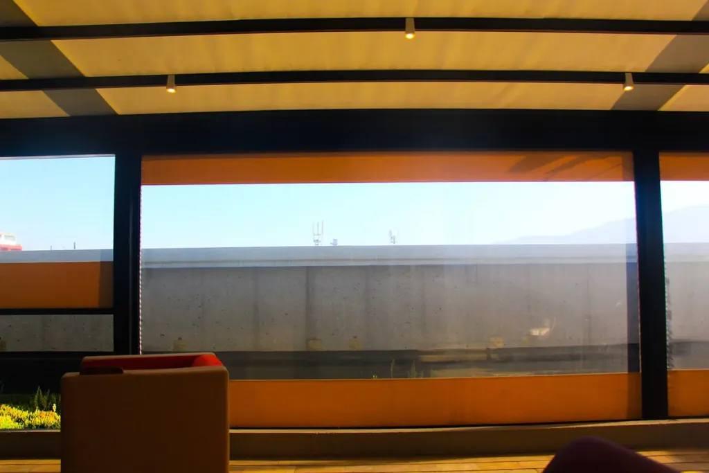 Vista desde el interior de una terraza cerrada con FlexiZipp, con el clear transparente bajado y la pérgola de madera encima