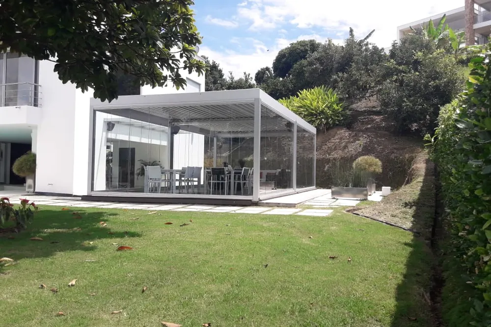 Pabellón acristalado con Slidinglass visto desde el jardín, entre árboles y seto perimetral