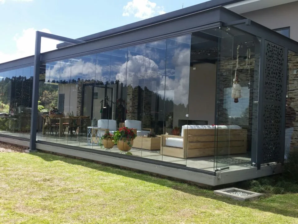 Pabellón cerrado con Slidinglass sobre el césped de una casa, con los paneles de vidrio corridos y la sala visible al fondo
