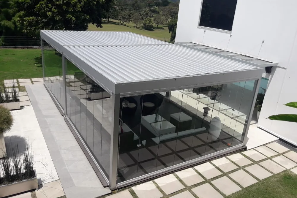 Pérgola bioclimática de lamas de aluminio cerrada en su perímetro con paneles de vidrio Slidinglass