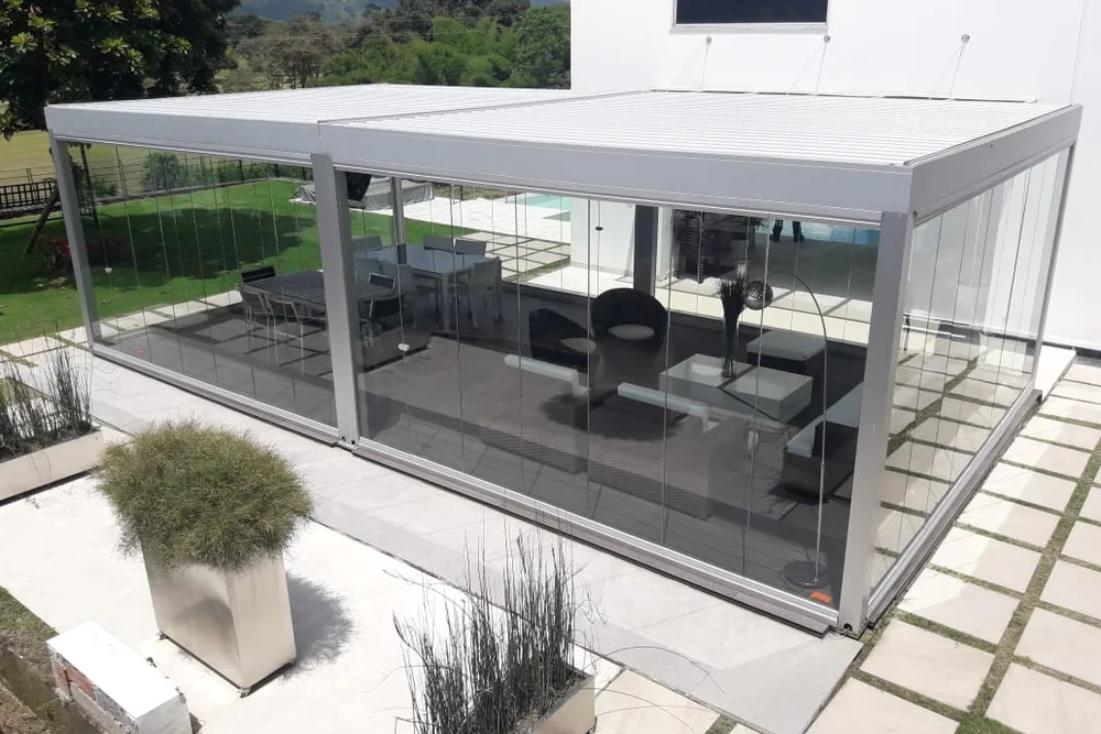 Sala exterior cerrada con Slidinglass junto a la piscina de una casa, con jardineras al costado