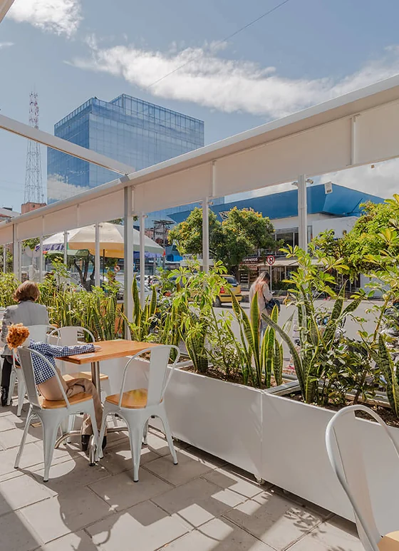 Terraza cubierta con cerramiento FlexiWind en vidrio y jardineras verdes