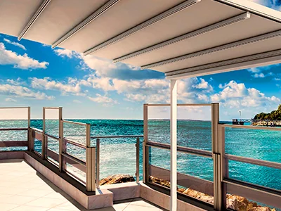 Paneles de vidrio FlexiWind sobre la baranda de una terraza cubierta por una pérgola, frente al mar