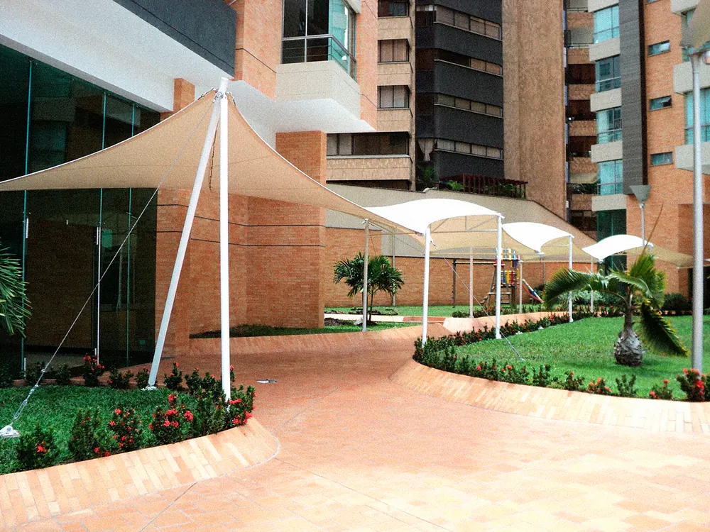 Serie de membranas autoportantes sobre el andén de acceso de un edificio en ladrillo, con jardín al costado