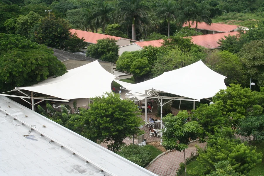 Vista aérea de dos membranas autoportantes cubriendo la zona de comidas de un campus, entre árboles