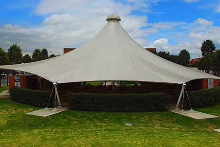 Membrana cónica de gran formato con seto perimetral, instalada sobre césped en un parque