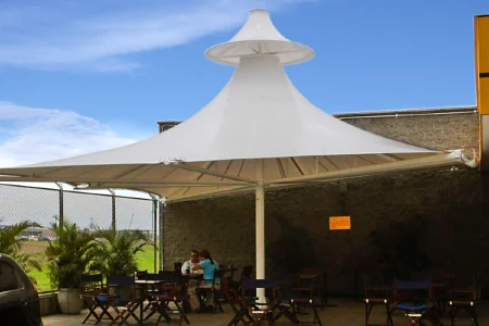 Membrana cónica cubriendo la terraza de mesas junto a la fachada de un local comercial