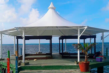 Membrana tipo kiosco sobre un muelle frente al mar, con mástiles perimetrales y cono central