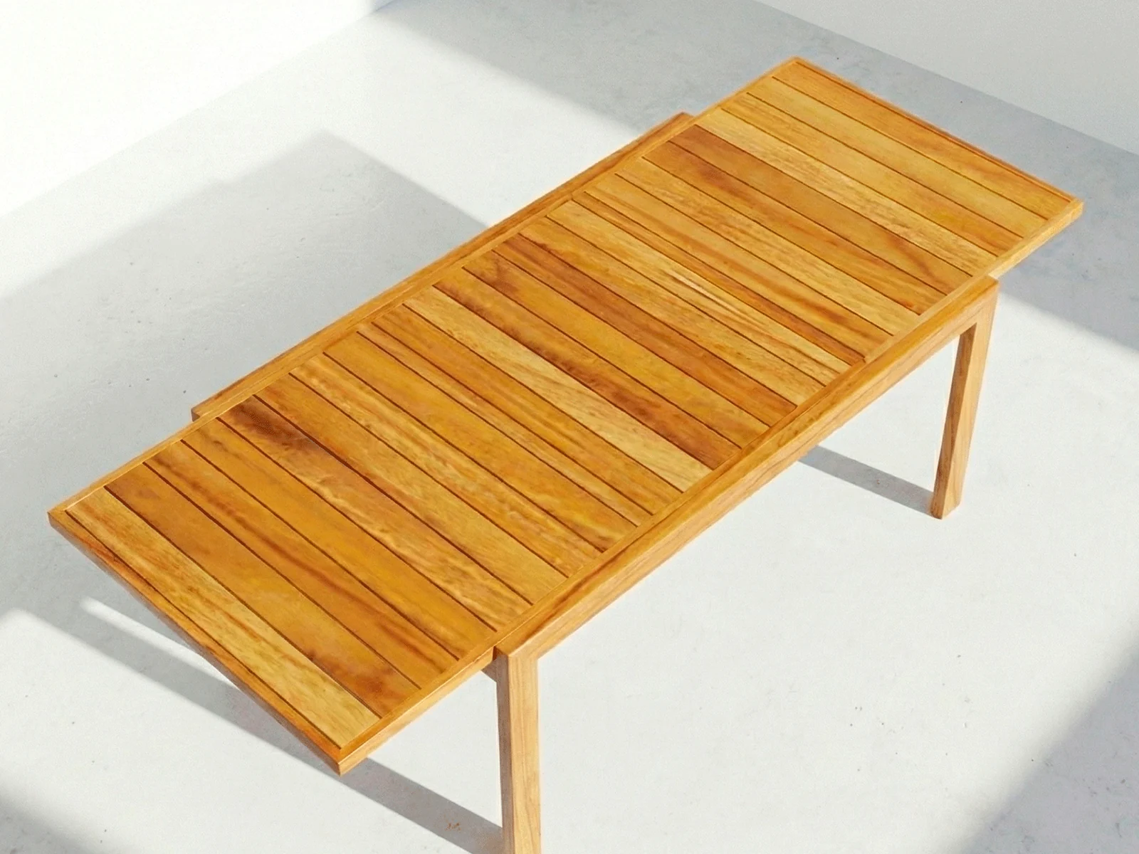 Mesa extensible Osaka en madera teca, vista en perspectiva sobre fondo blanco de estudio