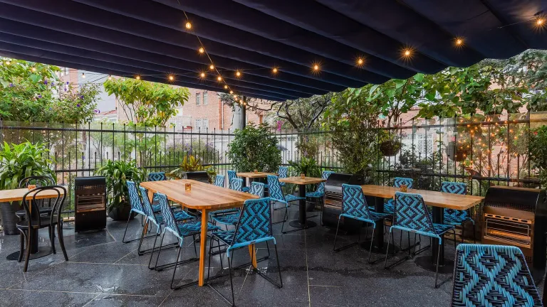 pérgola retráctil PergoFlex de lona azul desplegada sobre una terraza de mesas exteriores
