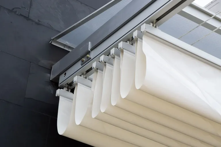 Detalle de la lona acrílica de una pérgola PergoFlex recogida en pliegues bajo el riel de aluminio