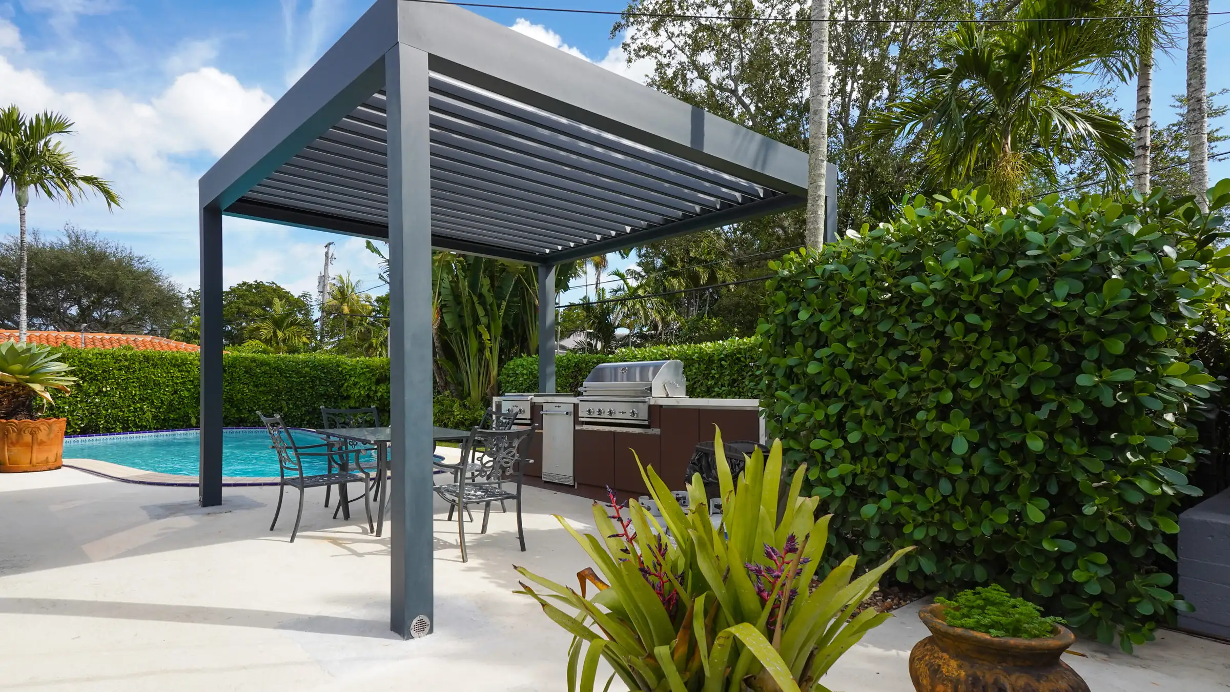 Pérgola bioclimática PergoLam tipo gazebo con lamas de aluminio orientables sobre una cocina exterior junto a la piscina