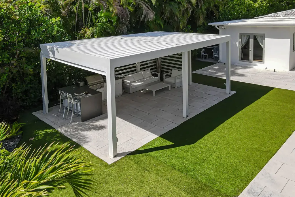 Pérgola bioclimática PergoLam blanca sobre una cocina exterior y una zona de estar en el jardín de una casa