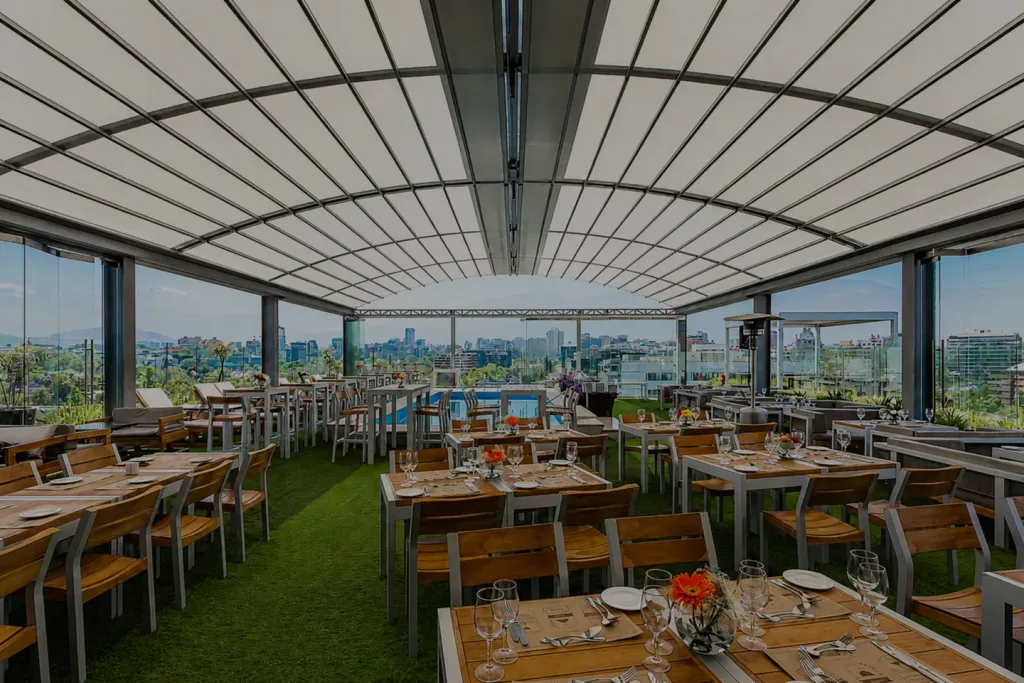 Pergola bioclimatica curva de aluminio y vidrio sobre una terraza rooftop con mesas de comedor y vista panoramica de ciudad