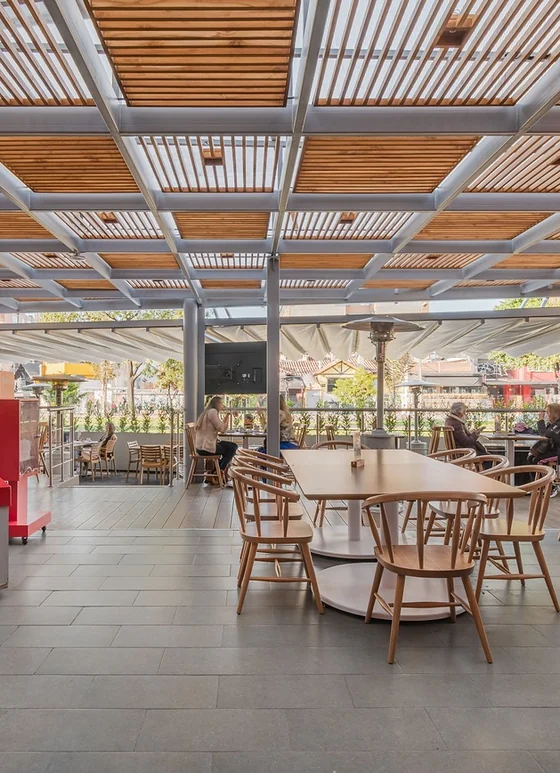 Pérgola fija de aluminio con listones de madera sobre una plazoleta de comidas