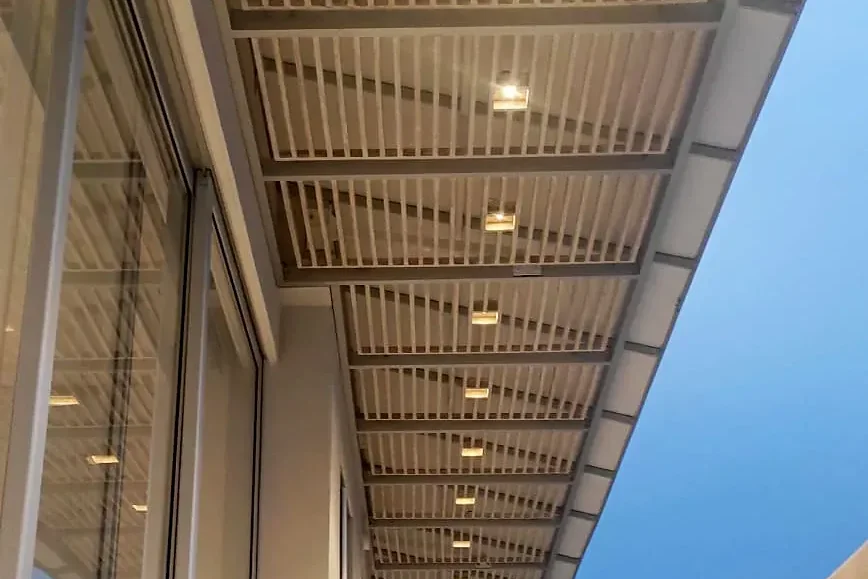 el cerramiento de vidrio corredizo Slidinglass bajo la pérgola fija, al atardecer y con las luces encendidas