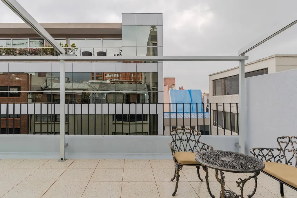 mesa y sillas del balcón bajo la estructura de aluminio de la pérgola retráctil recogida