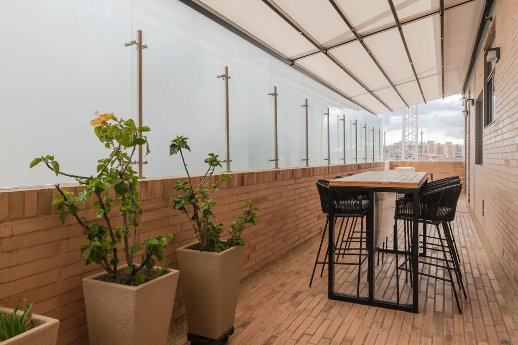 pérgola retráctil desplegada sobre el balcón corrido de un edificio residencial, con mesa alta y taburetes