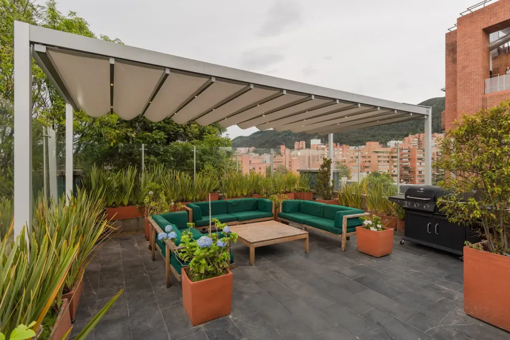 pérgola retráctil desplegada sobre la zona de estar de la terraza, con la ciudad y los cerros al fondo