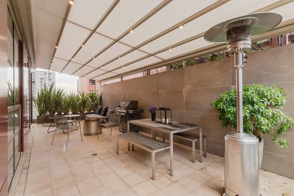 asador y mesa comunal de la terraza bajo la pérgola retráctil desplegada, en Bogotá