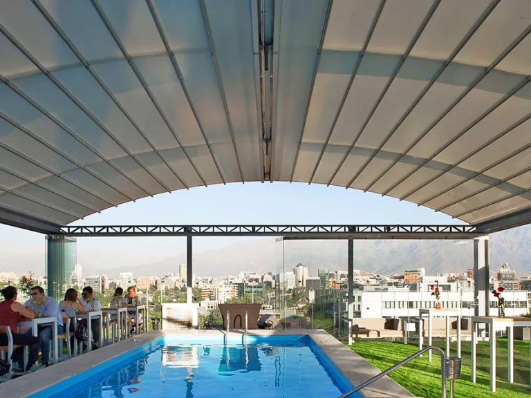 Pérgola retráctil PergoDom con la lona tensada sobre el arco, en la terraza de una piscina
