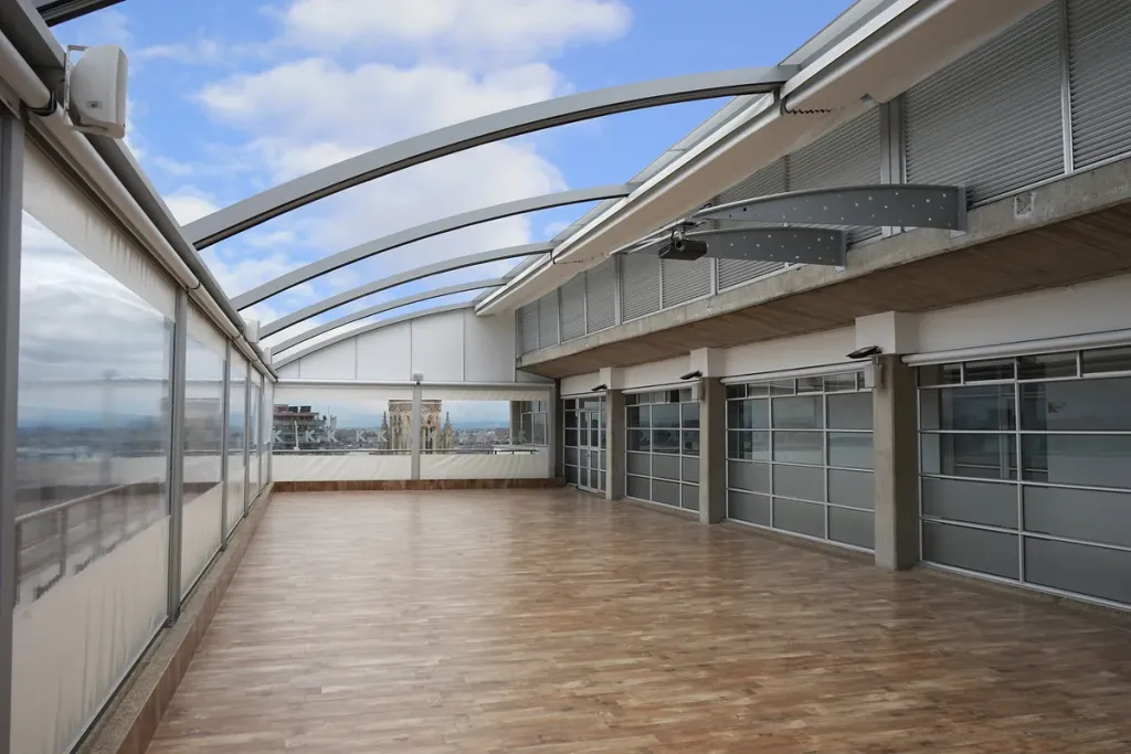 Pérgola retráctil PergoDom sobre una terraza con deck de madera y cerramiento en vidrio, Bogotá