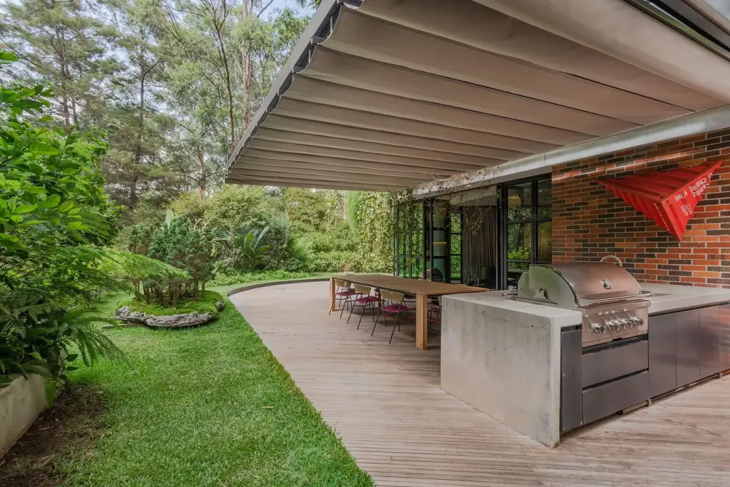 Pérgola retráctil PergoFlex vista desde el césped del jardín de una vivienda, con la lona desplegada