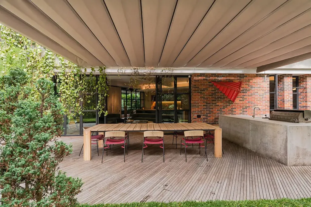 Pérgola retráctil PergoFlex con la lona extendida sobre un comedor exterior junto al césped