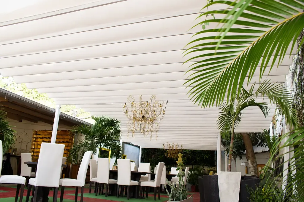 Pérgola retráctil PergoFlex de lona blanca sobre el comedor exterior de un restaurante entre palmeras
