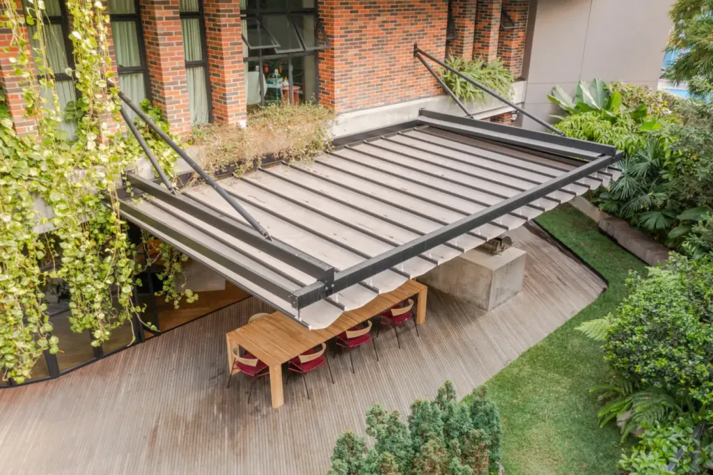 Pérgola retráctil PergoFlex suspendida con tensores sobre un patio, con la lona recogida en pliegues
