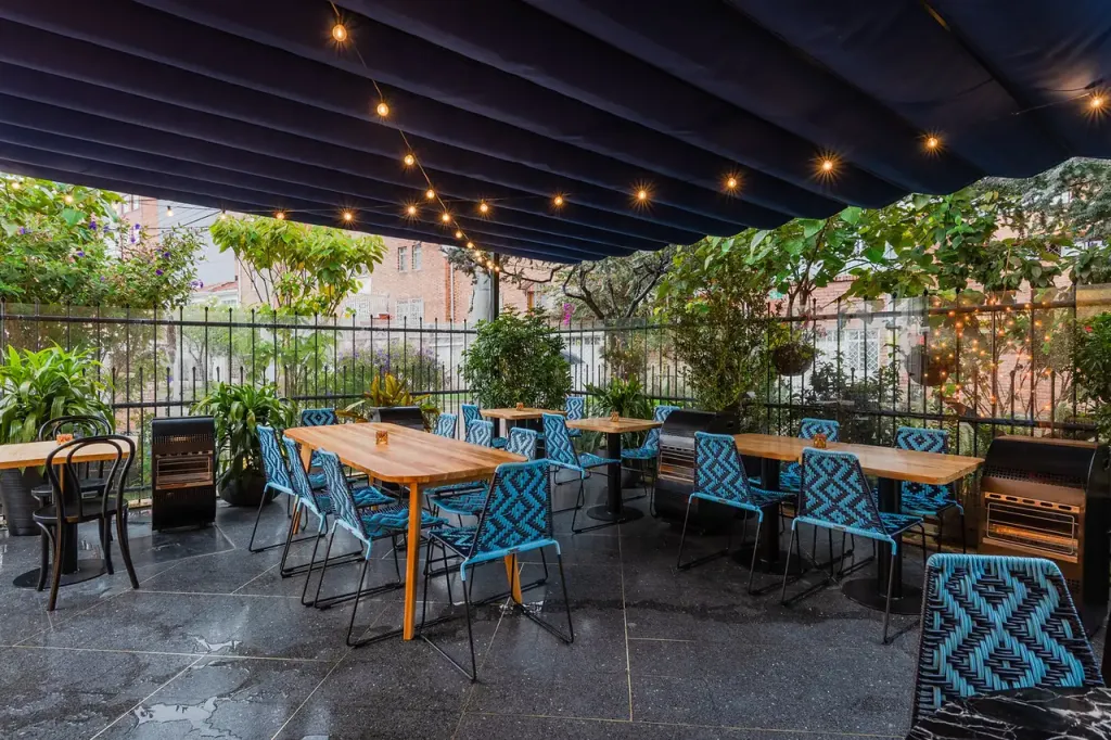 Pérgola retráctil PergoFlex de lona oscura con guirnaldas de luces sobre la terraza de un restaurante