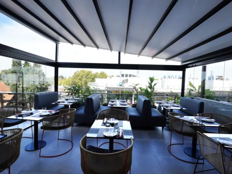 Pérgola retráctil PergoTek Classic parcialmente abierta sobre el comedor de un restaurante en rooftop