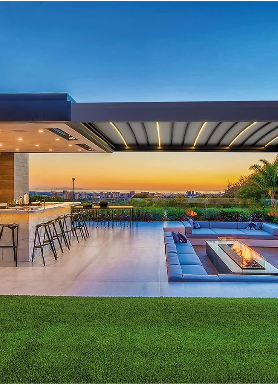 Pérgola PergoTek Design sobre una terraza con barra y chimenea, al atardecer