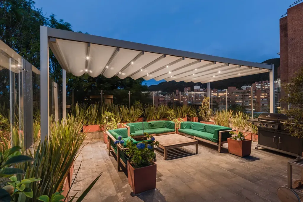 Pérgola PergoTek Romano sobre la terraza de una vivienda con jardineras y zona de estar