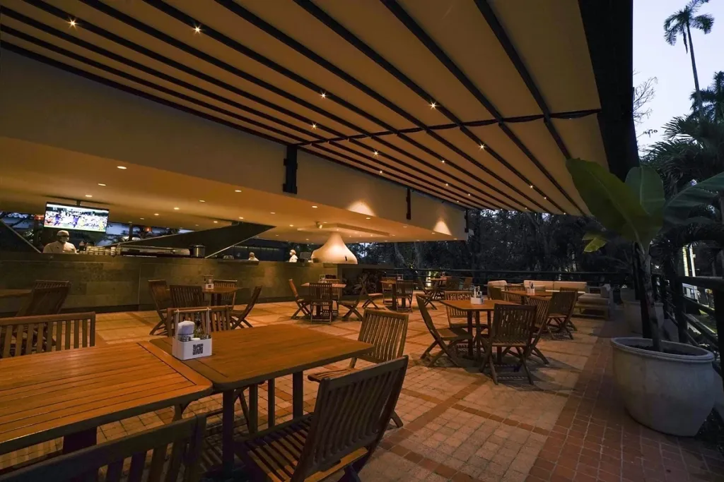 Terraza de club cubierta con pérgola retráctil PergoTek y mobiliario de madera