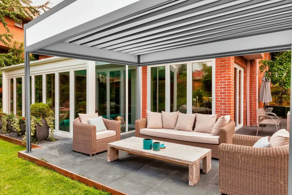 Pérgola retráctil PergoTek Deco con la lona recogida en ondas sobre una terraza de jardín con sofás de fibra