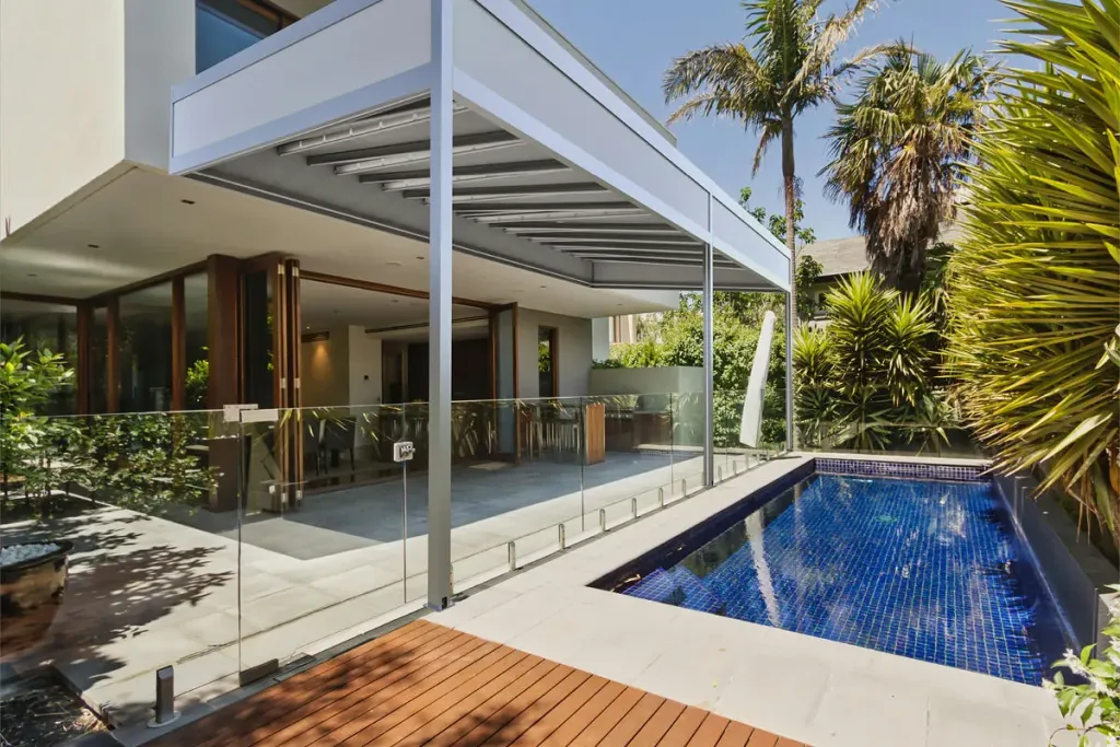 Pérgola retráctil PergoTek Deco con la lona tensada y plana sobre la terraza de una casa junto a la piscina