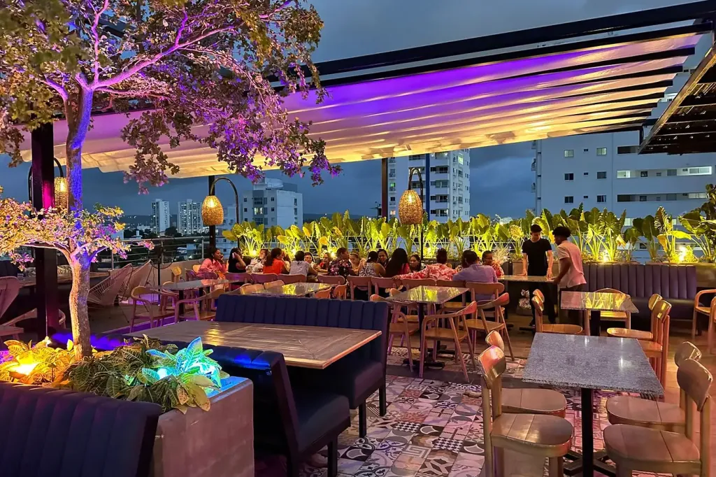 terraza de noche bajo la pérgola retráctil PergoTek, con el arbolado iluminado y las mesas ocupadas