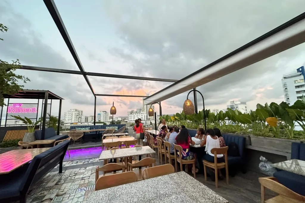 pérgola retráctil con la lona recogida sobre las mesas de la terraza, con el cielo del atardecer a la vista