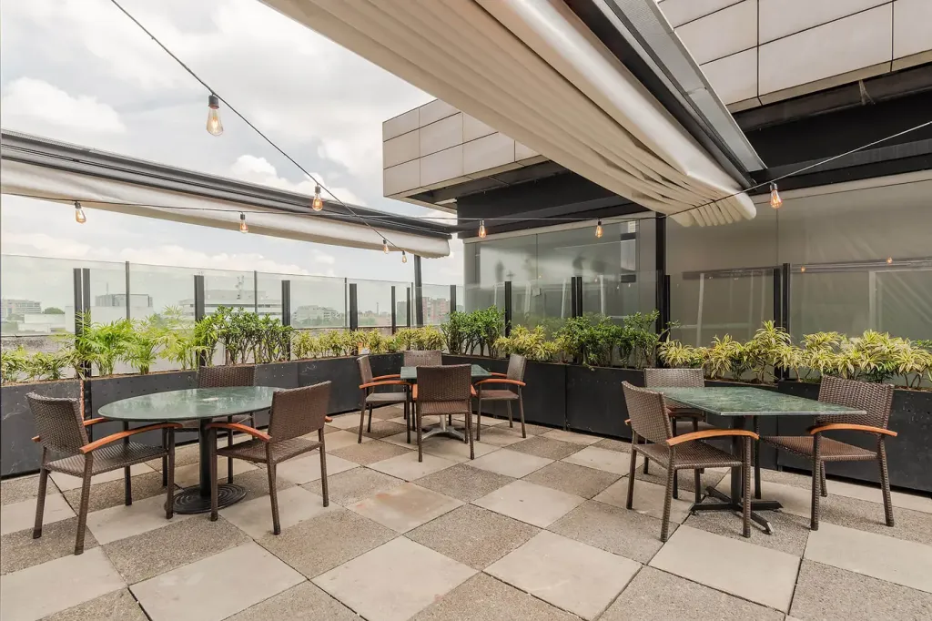 mesas de la terraza bajo el alero de la cubierta retráctil, junto a la baranda de vidrio y las jardineras