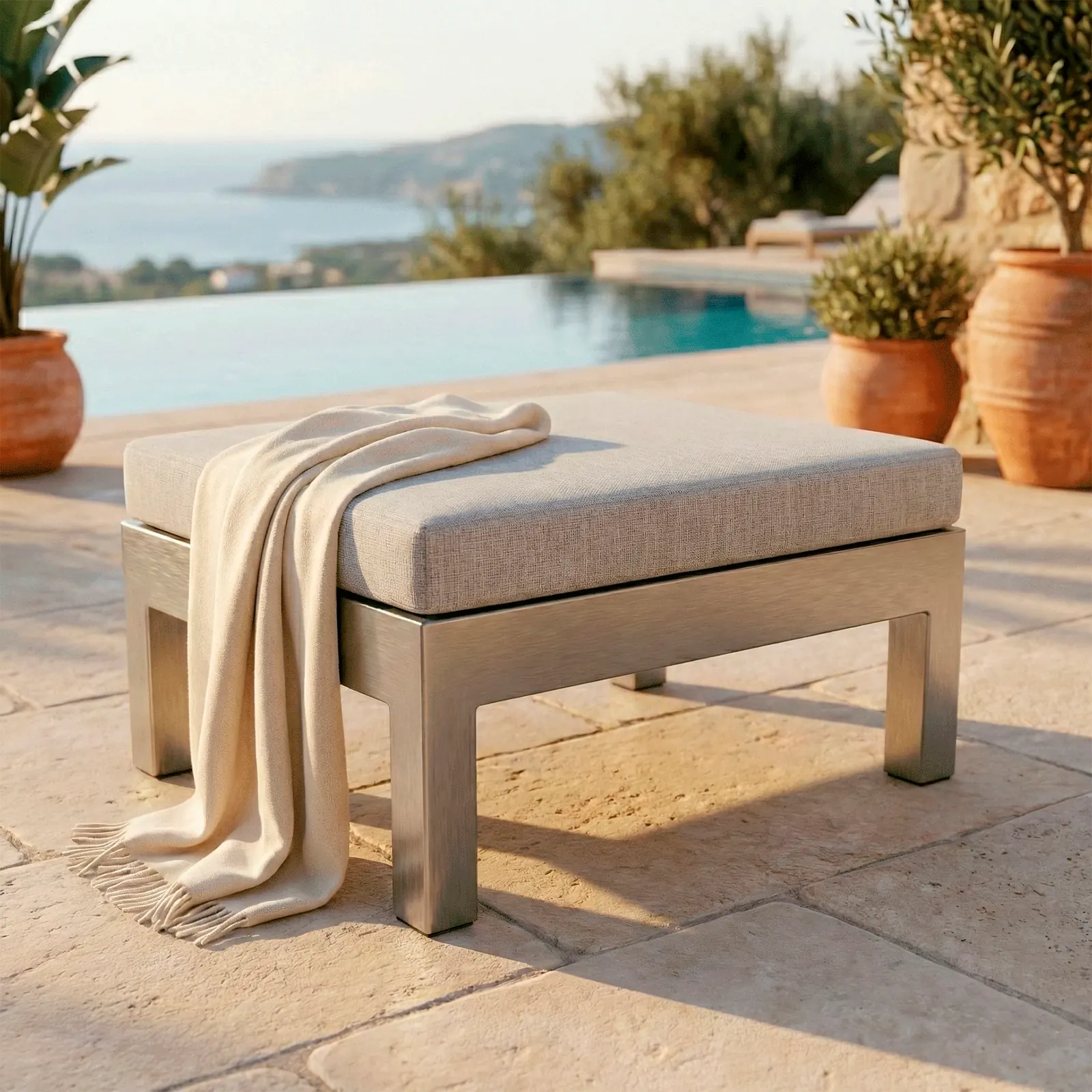 Pouf Montecarlo en aluminio con cojín, junto a un sofá en una sala luminosa