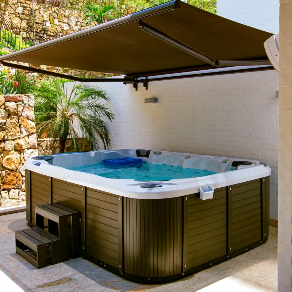 Sombralina de brazos invisibles desplegada sobre un jacuzzi exterior, con los brazos y el tubo enrollador a la vista