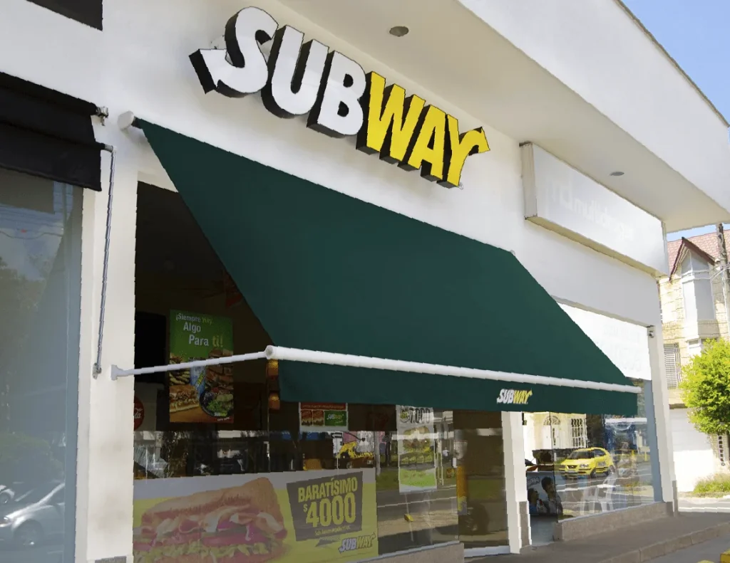 Toldo enrollable Baneta proyectante en lona verde extendido sobre la vitrina de un local Subway en Bogotá