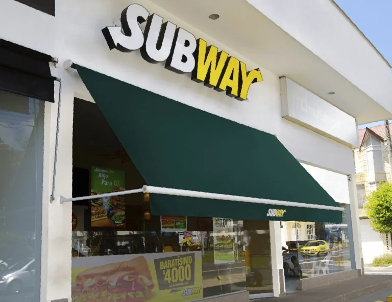 Toldo enrollable Baneta proyectante en lona verde extendido sobre la vitrina de un local Subway en Bogotá