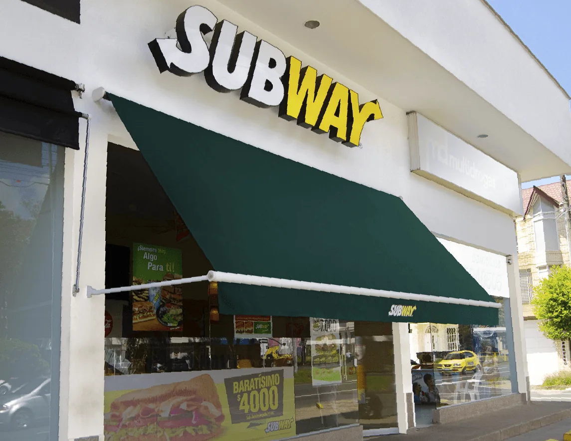 Toldo enrollable Baneta proyectante en lona verde extendido sobre la vitrina de un local Subway en Bogotá