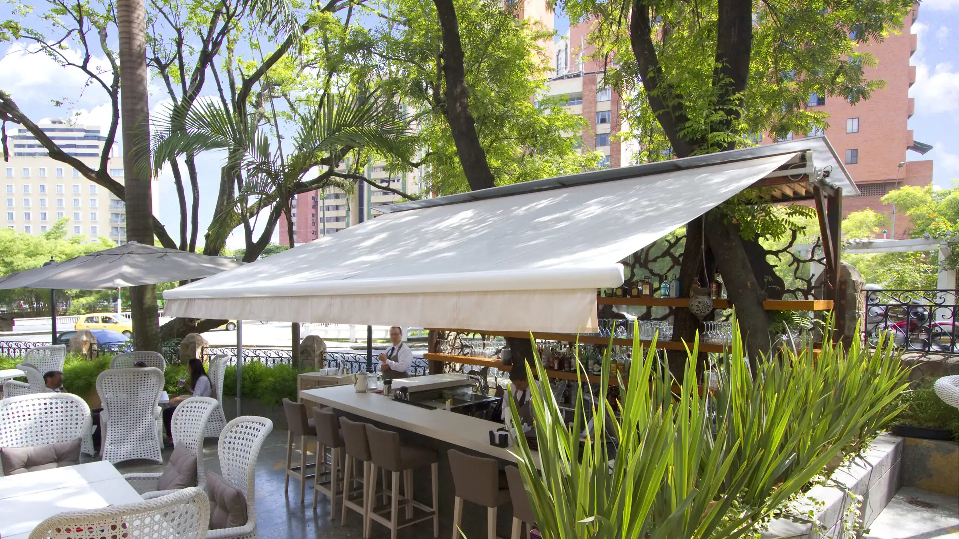 Toldo retráctil de lona crema sobre la barra de una terraza al aire libre entre árboles