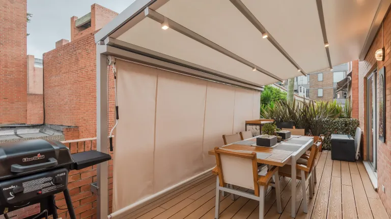 Toldo vertical Baneta Vertical de lona beige cerrando el lateral de una terraza residencial con deck de madera en Bogotá