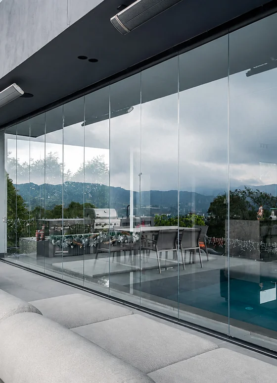 Cerramiento FlexiGlass en vidrio plegable entre la sala exterior y la piscina de una casa